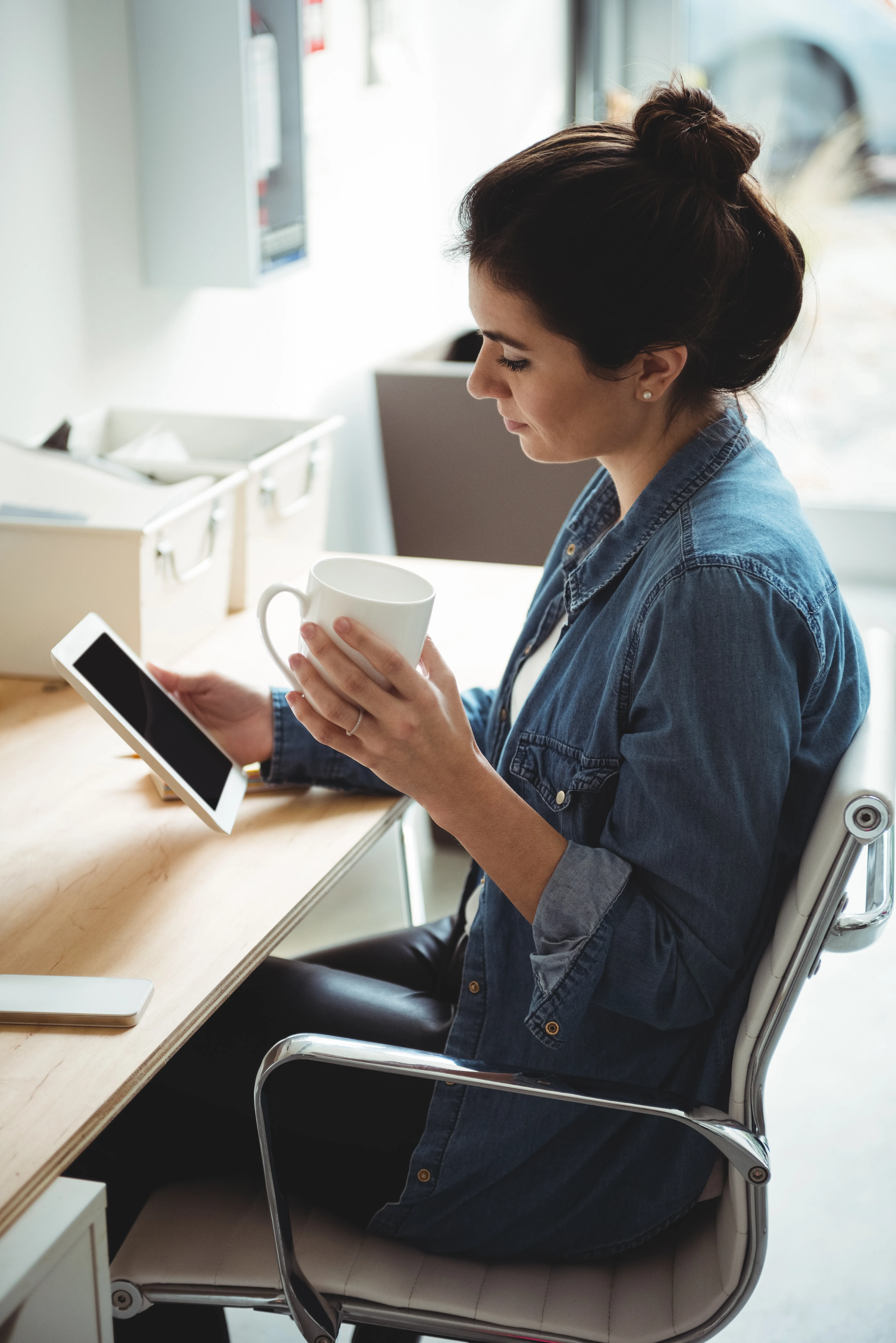 Mulher usando tablet enquanto toma café em mesa de trabalho